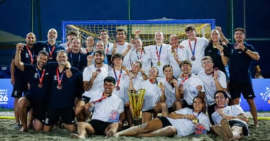 A beach soccer team poses triumphantly on the sand with their medals and trophy, celebrating a victory under stadium lights.