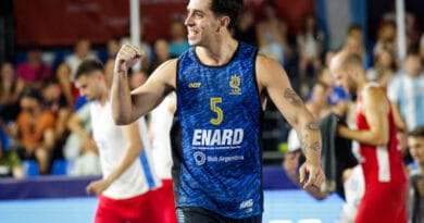 A basketball player in a blue jersey with the number 5 celebrates with a raised fist on the court.