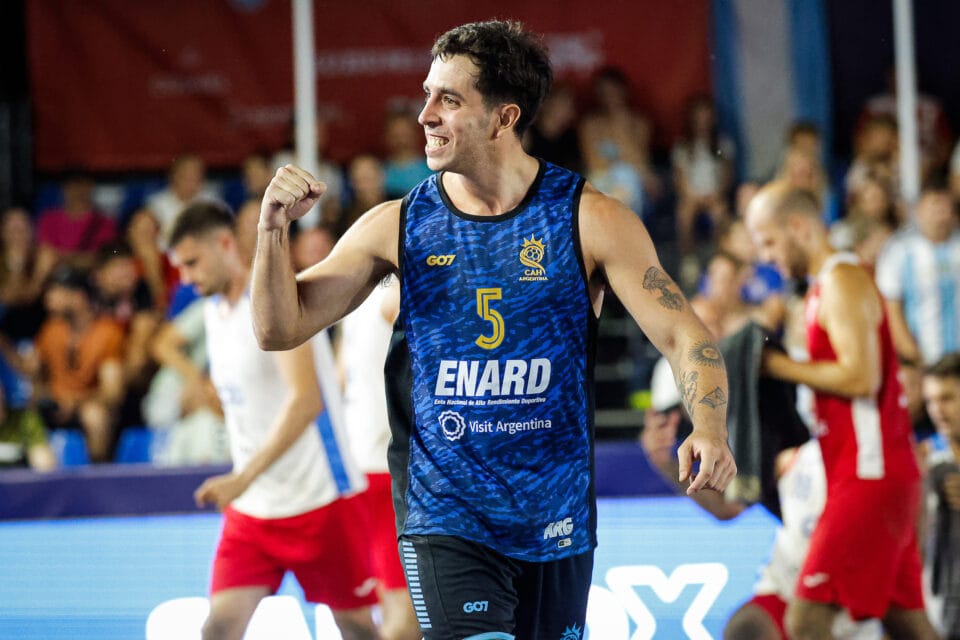 A basketball player in a blue jersey with the number 5 celebrates with a raised fist on the court.